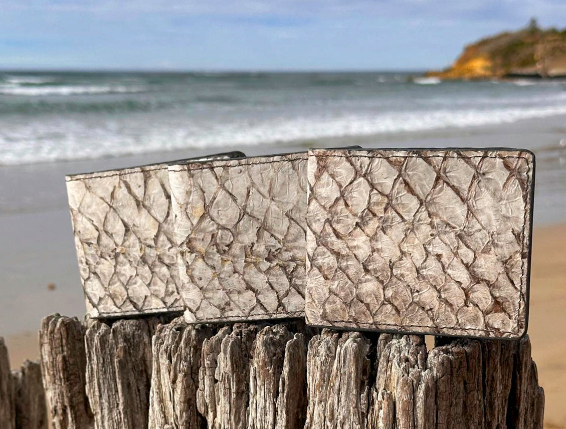 Three of Maugro's bi-fold wallets sitting atop a post overlooking the beach