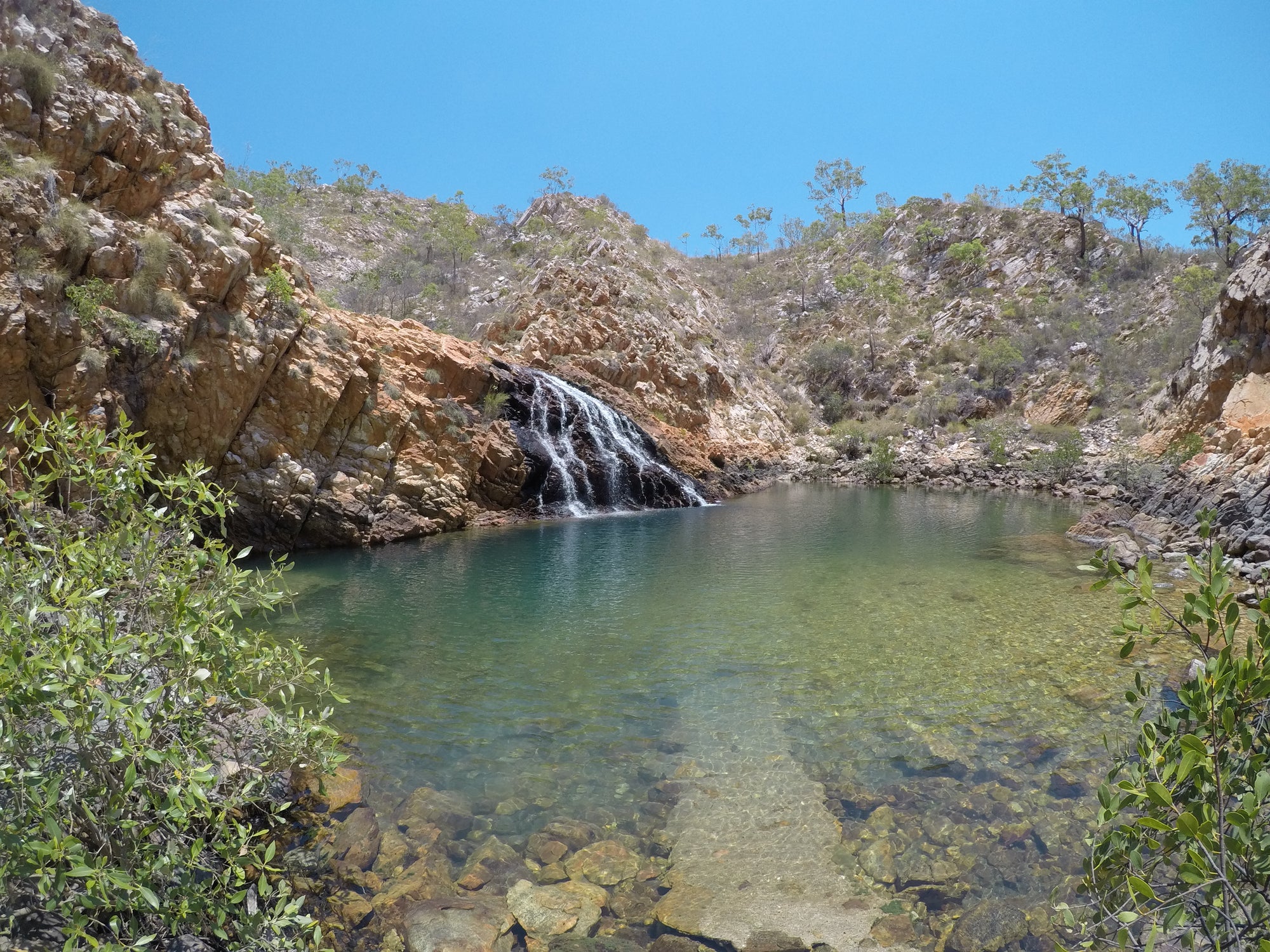 Waterfall flowing into a pool surrounded by rocky cliffs and greenery