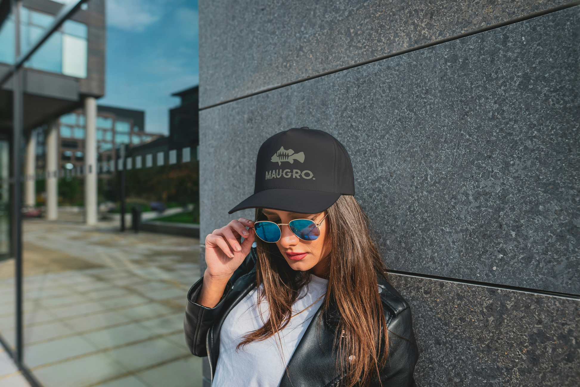 Black Maugro cap with green logo worn by a woman with long hair and sunglasses outdoors.