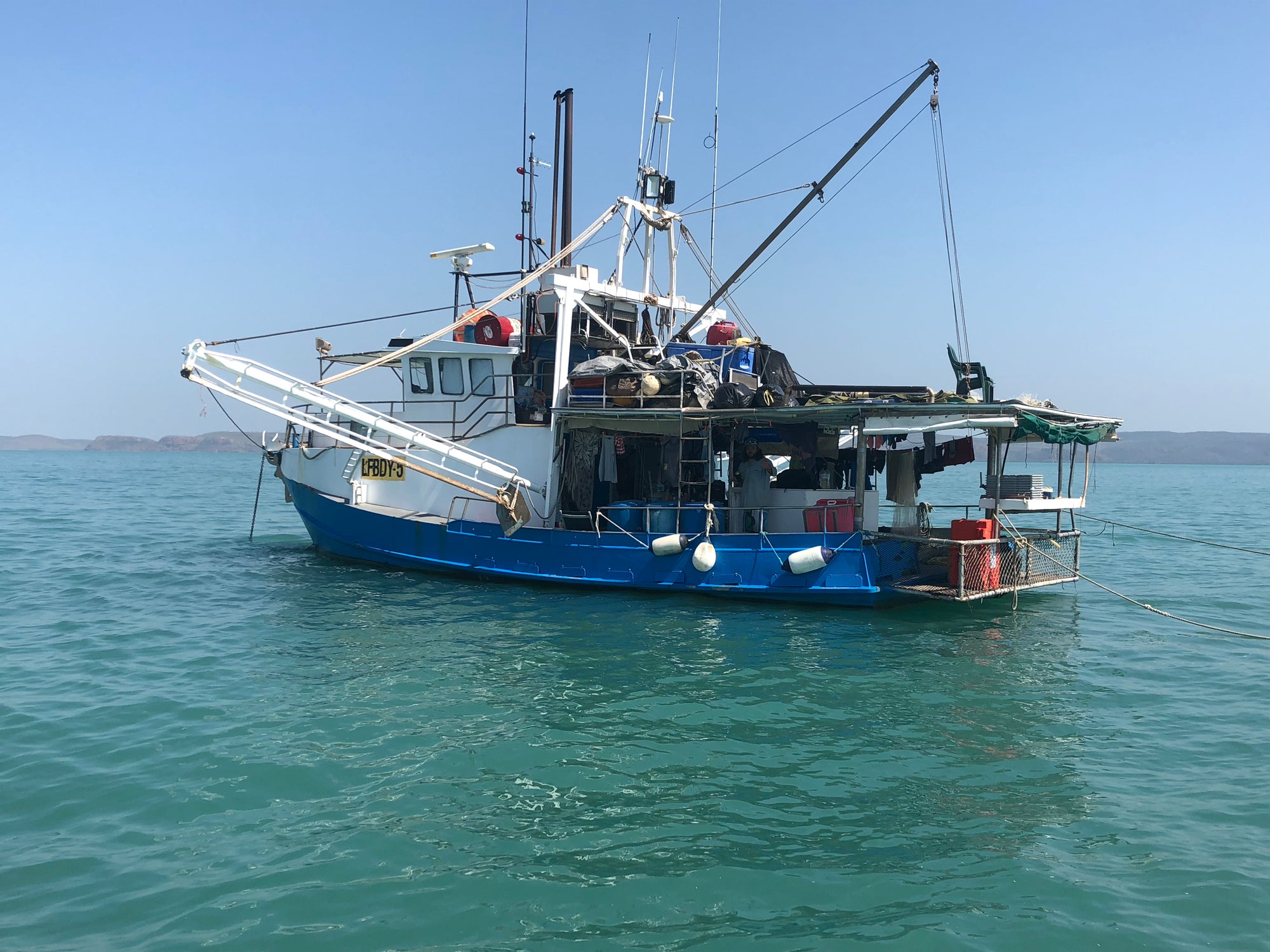 Blue fishing boat on calm water with clear sky