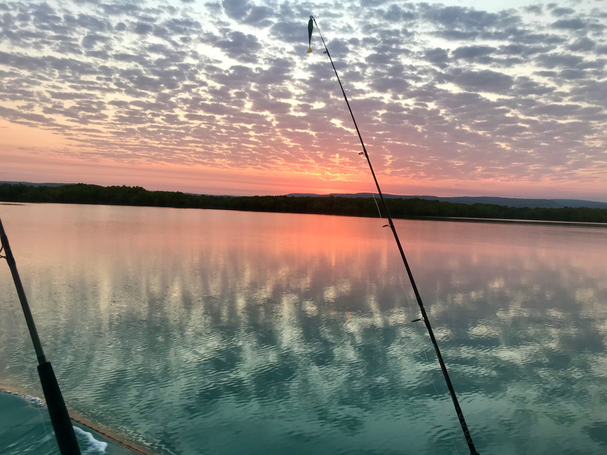 Fishing rod over calm water with a colorful sunset sky