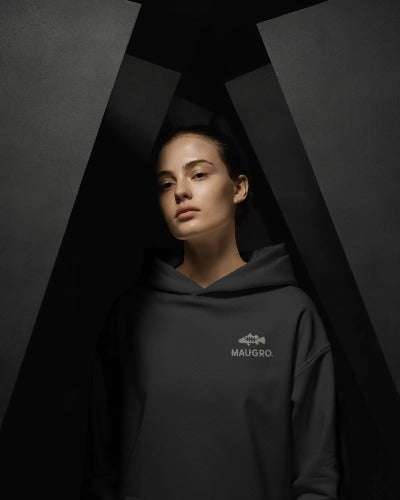 Black unisex hoodie with subtle MAUGRO logo on chest, worn by model against dark background.